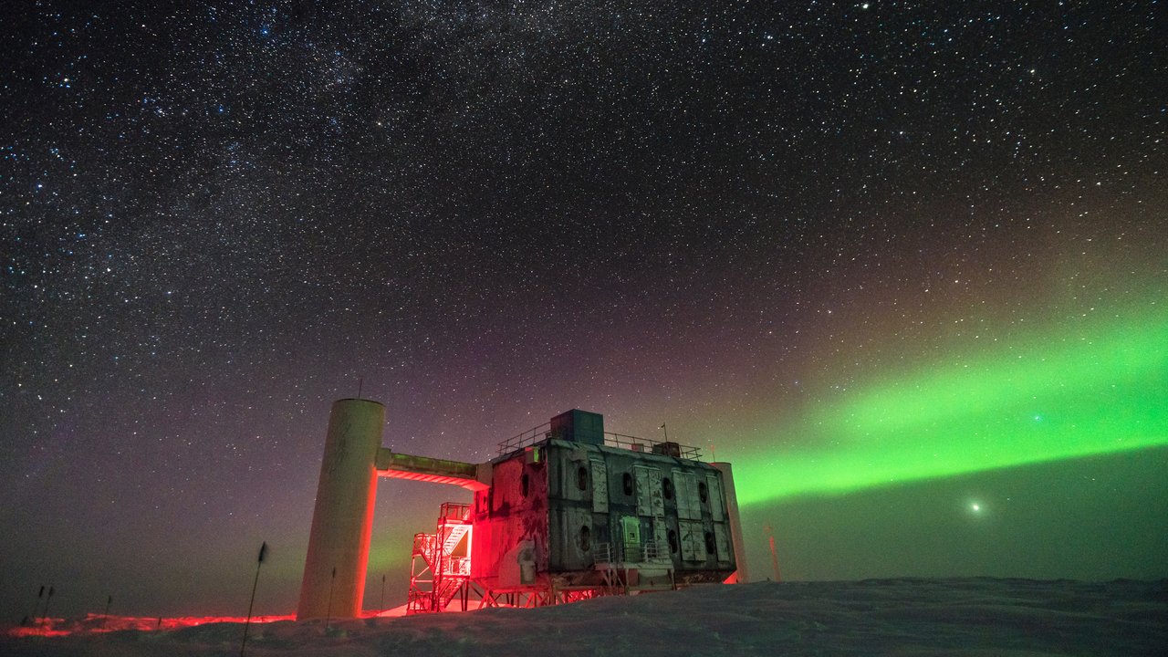 Forschungsstation, von der rotes Licht ausgeht, steht in einer nächtlichen Polarlandschaft; am Himmel Nordlicht 