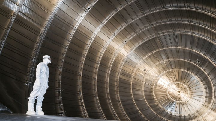 Ein in einem weißen Reinraumanzug gekleideter Wissenschaftler steht in einer sehr großen tunnelartigen Röhre