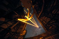 Wir befinden uns im Inneren des Hauptteleskops Yepun und blicken durch einen geöffneten Spalt nach oben. Ein Bündel aus vier leuchtenden Laserstrahlen zielt vom Inneren des Teleskops in den Nachthimmel.