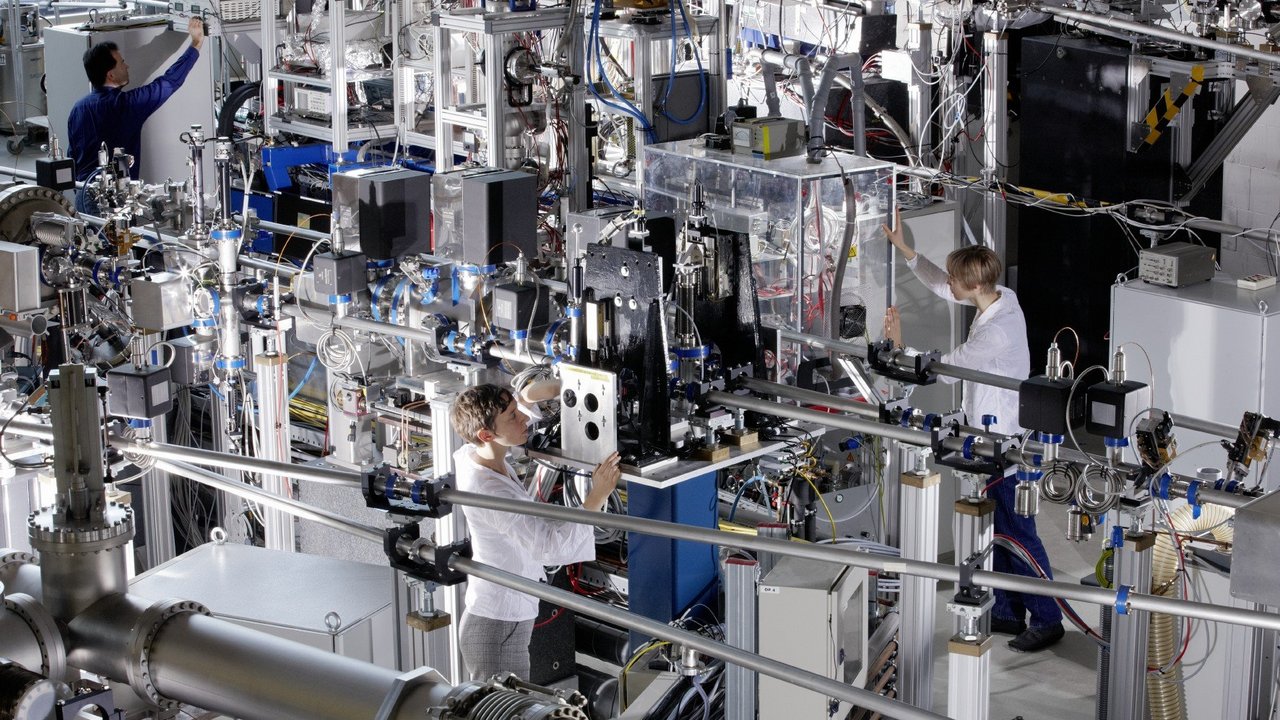 Wissenschaftlerinnen und Wissenschaftler arbeiten in einem Raum voller Maschinen, Laseraufbauten