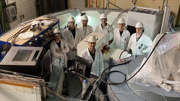 Wissenschaftlerinnen und Wissenschaftler in weißen Laborkitteln umgeben von technischen Anlagen