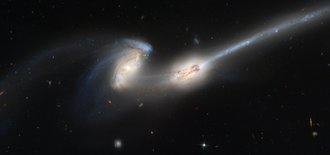 Zwei spiralförmige helle Galaxien vor dunklem Sternenhimmel, die Arme der Spiralgalaxien überlappen.