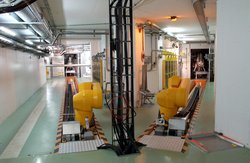 Zwei fahrbare Industrieroboterarme im ISOLDE-Strahlenschutzbereich. Hinter jedem Roboter führt eine lange Schiene durch einen Gang zu den Metallcontainern, in denen sich das Target-Material befindet.
