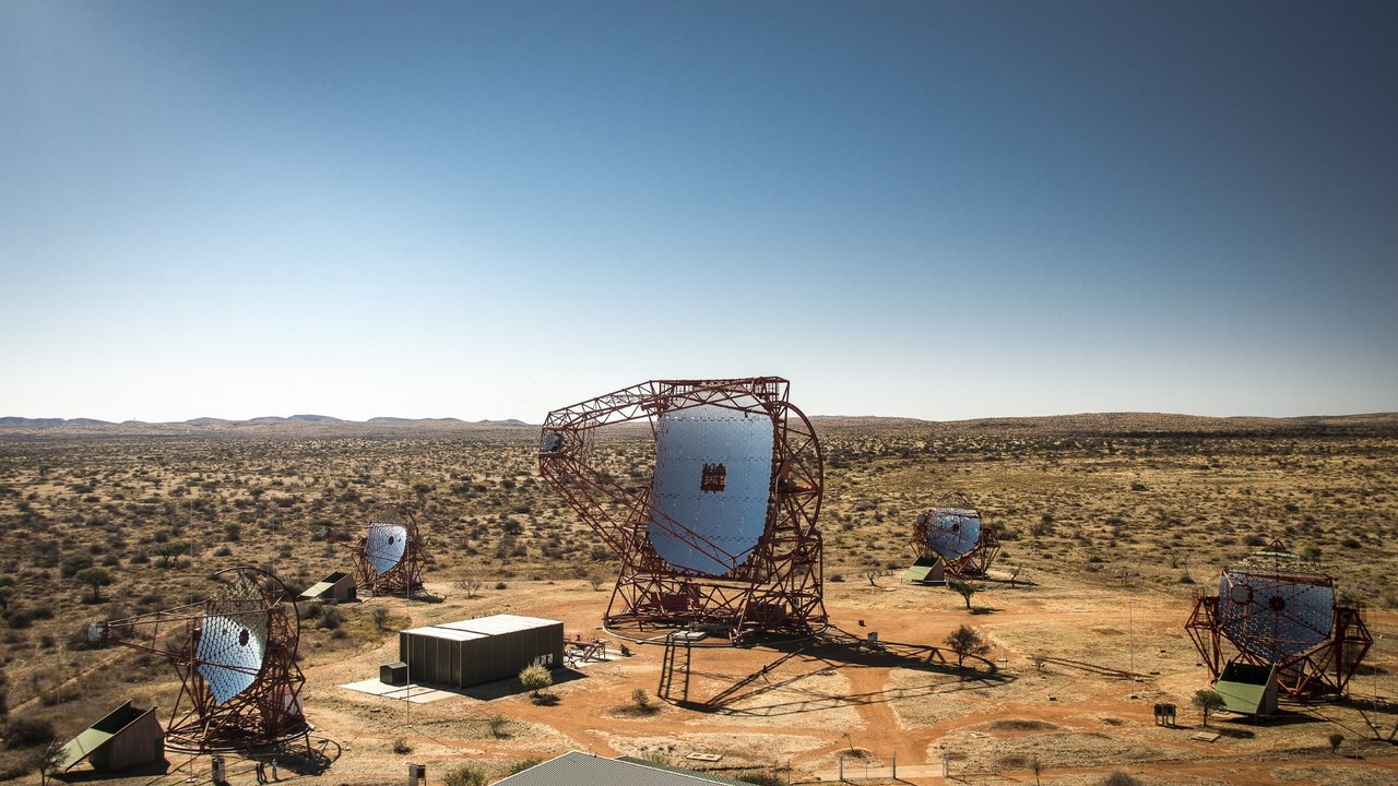 Vier kleine und ein großes Teleskop aus Gerüsten und zahlreichen Segmentspiegeln in einer Wüstenlandschaft