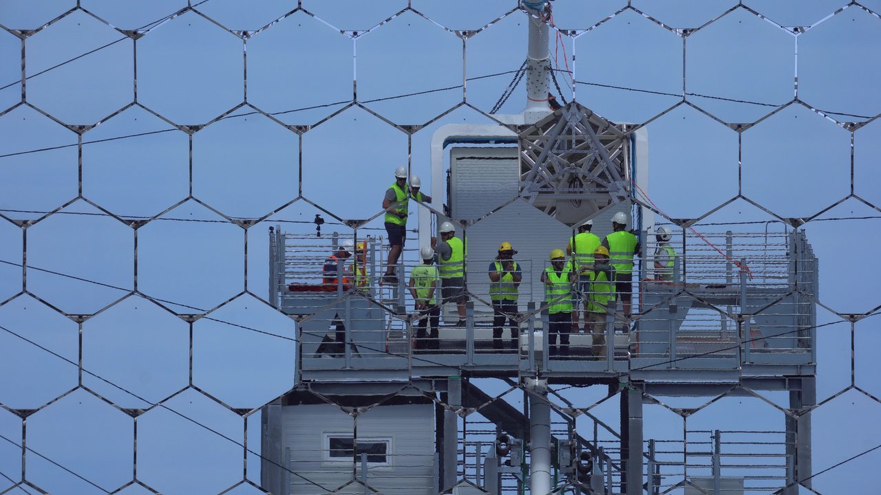 Mehrere Arbeiter auf einer Stahlplattform durch ein Gitter fotografiert