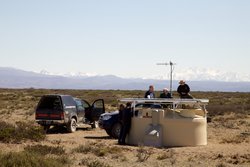 Im Vordergrund befindet sich ein zylinderförmiger, beiger Wassertank mit einem Aufsatz, an dem Wissenschaftler arbeiten. Daneben ist ein Auto geparkt. Am Horizont sind in der ferne Berge auszumachen.