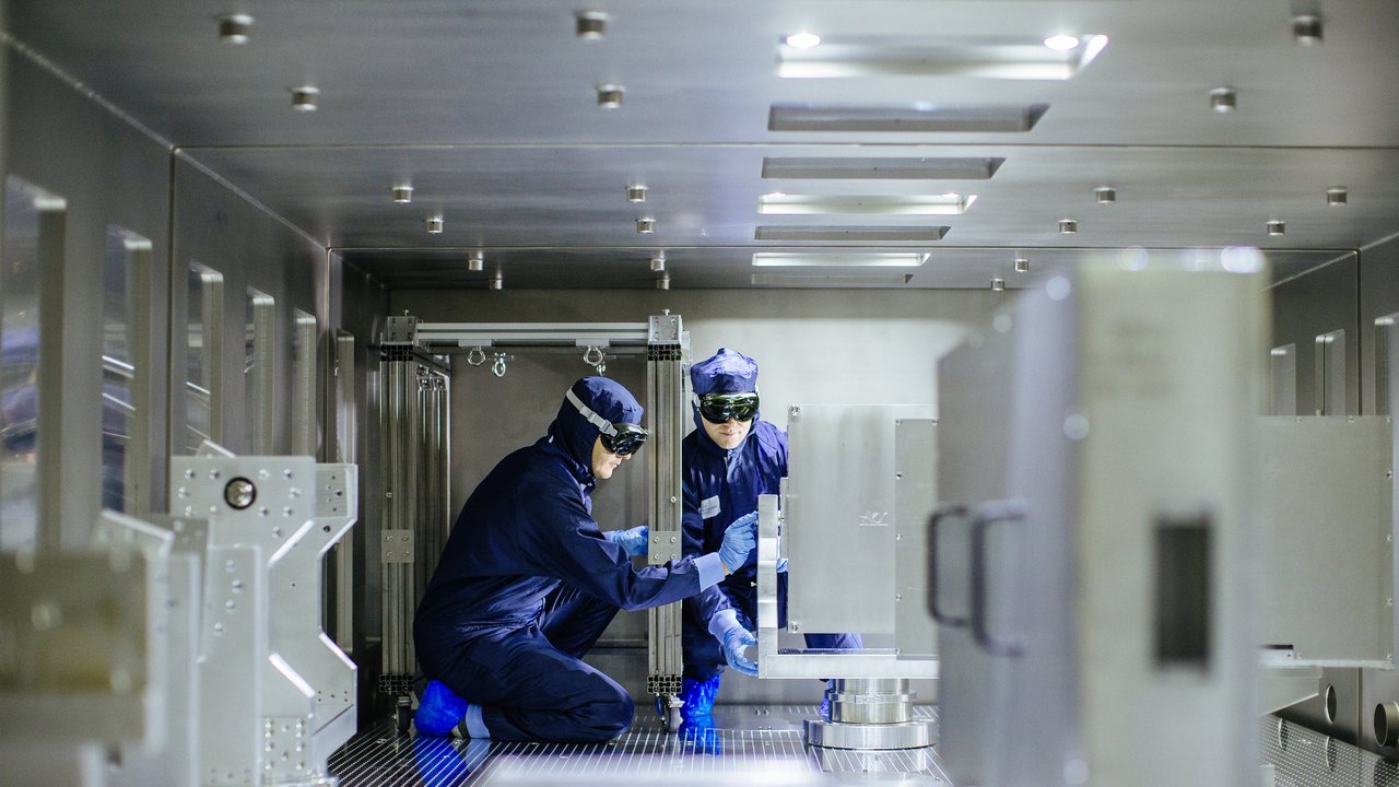 Zwei Wissenschaftler in Schutzanzug und mit Schutzbrille arbeiten auf einem metallenen Steg