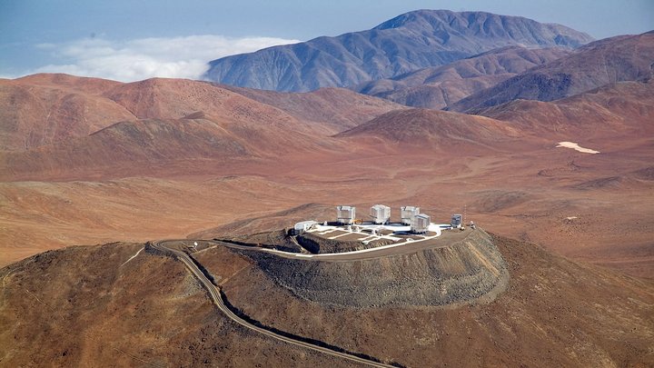 Inmitten einer Wüste ragt ein Hügel heraus, auf dem einige Teleskope stehen.