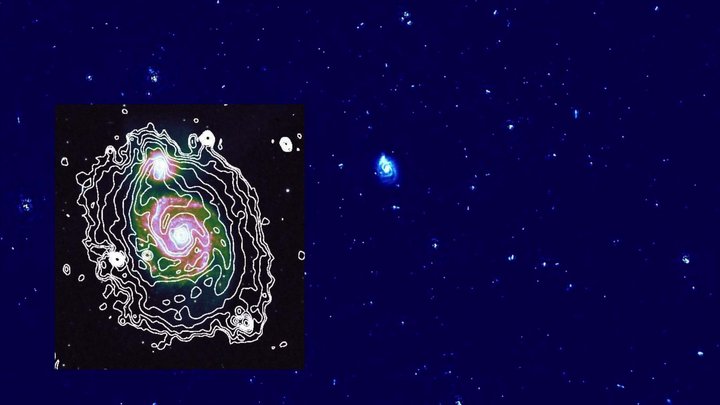 Dunkler Hintergrund. In der Mitte ist eine kleine helle Spiralgalaxie zu sehen. Darum herum viele kleinere helle Flecken.