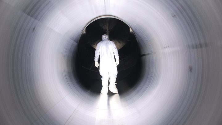 Ein Mann in einem weißen Schutzanzug läuft durch eine weiße Röhre auf ein dunkles Ende des Tunnels zu.