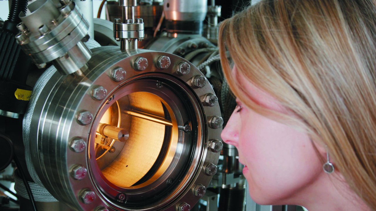 Wissenschaftlerin schaut in die runde Öffnung einer Apparatur