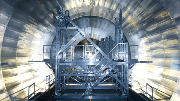 Das Foto zeigt drei Personen in Schutzanzügen, die auf einem Gerüst im Inneren des Experiments stehen.