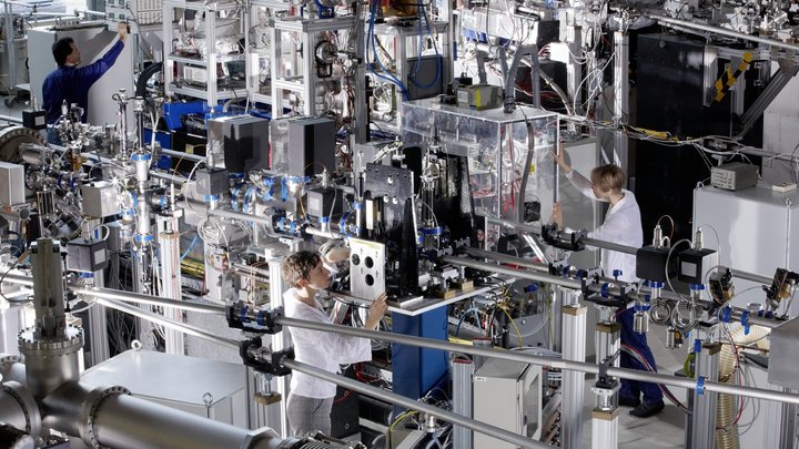 Wissenschaftlerinnen und Wissenschaftler arbeiten in einem Raum voller Maschinen, Laseraufbauten